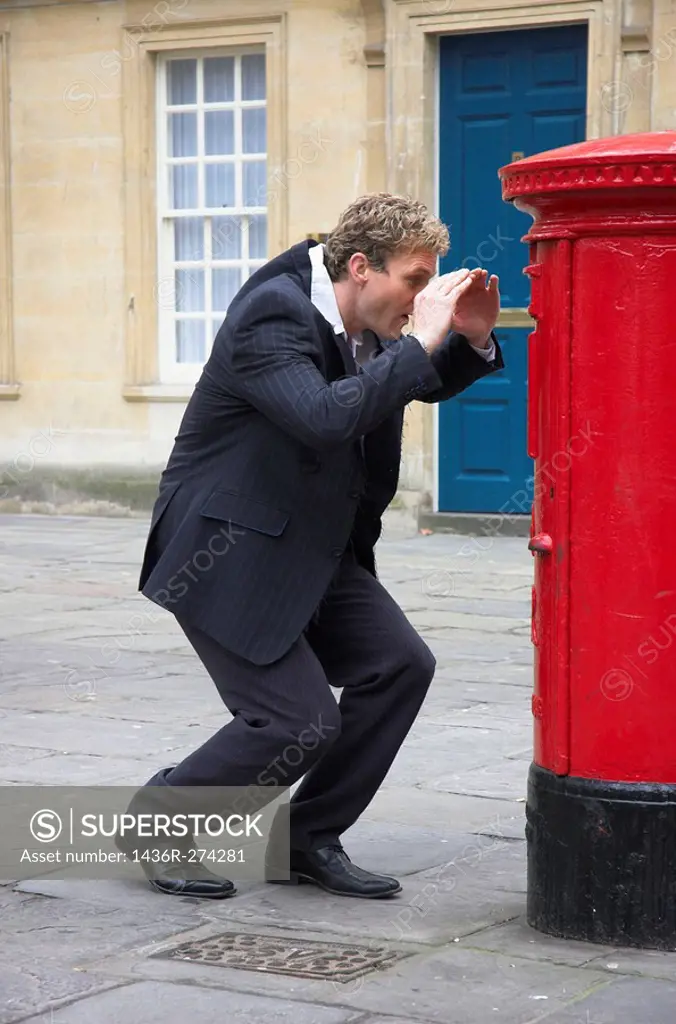Young businessman trying to llok into a British Royal Mail post box.
