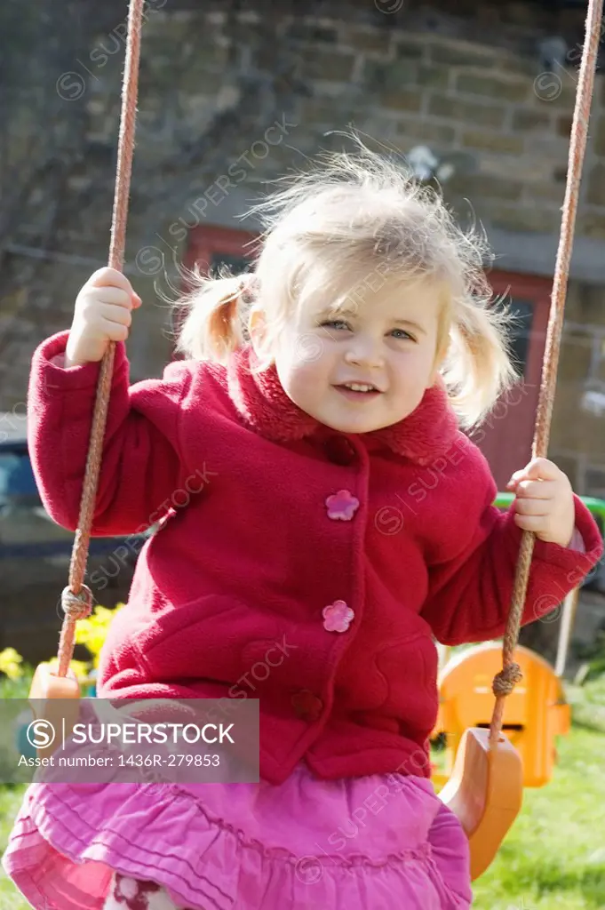 3 year old girl swinging outside, smiling into camera, with bunches
