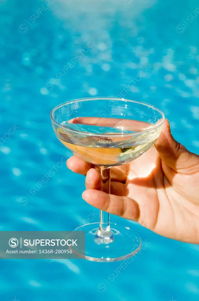 Hand holding champagne glass in front of pool.