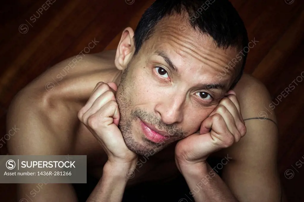 Hispanic man, sitting on a wood floor, posing without a shirt
