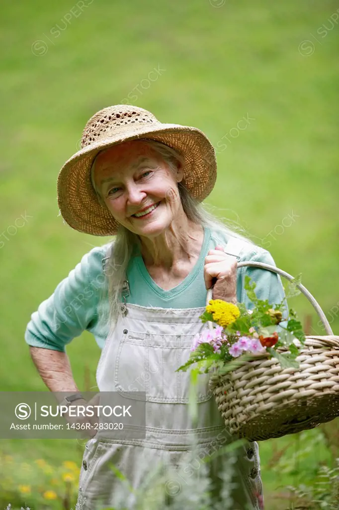 Senior woman with straw hat looking into camera with basket of flowers