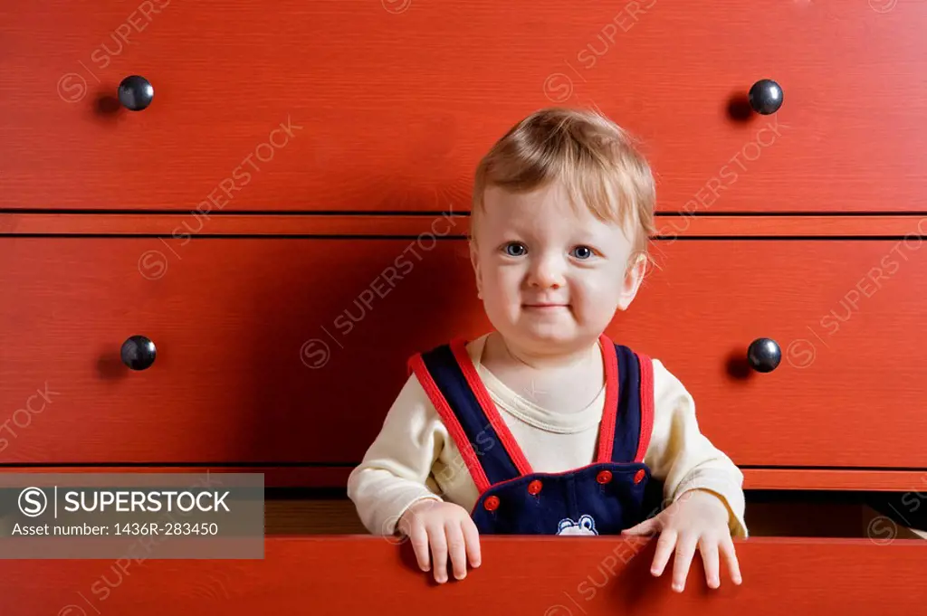 Baby boy playing inside cupboard drawer