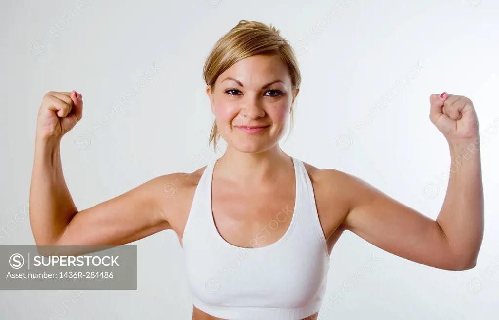 Young blond woman in workout gear happily flexes her muscles.