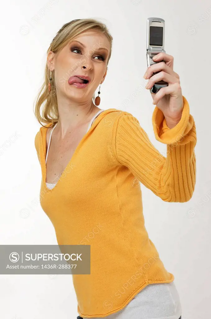 Blond woman, sticking her tongue out taking a picture of herself with a cell phone