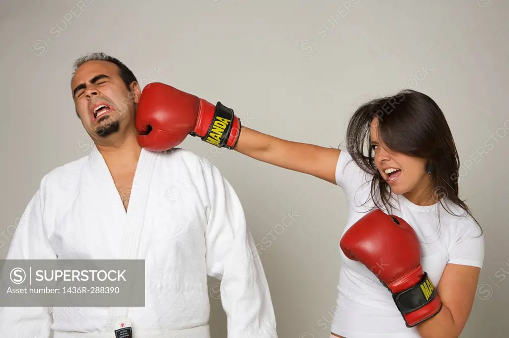 Latin woman wearing boxing gloves throwing punch at her husband