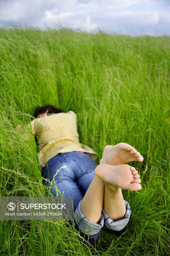 Young barefooted woman resting on a peaceful field of grass