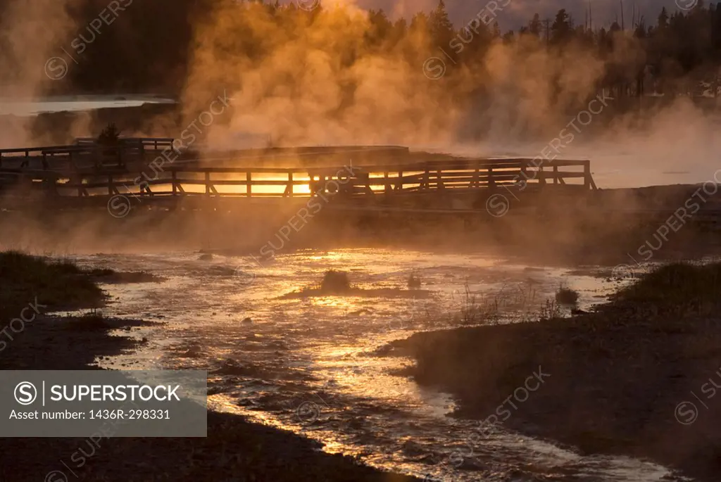 The setting sun reflecting on Firehole Lake geothermal area and boardwalk suggests a boiling pool of magma below