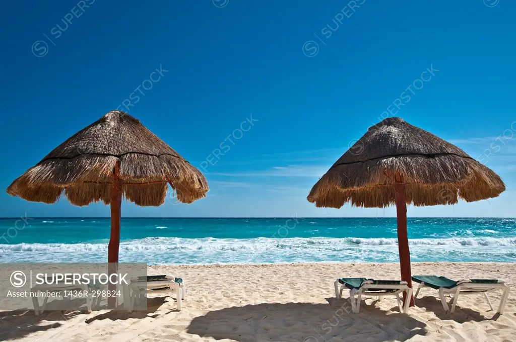 Two straw sun umbrella by a white sandy beach