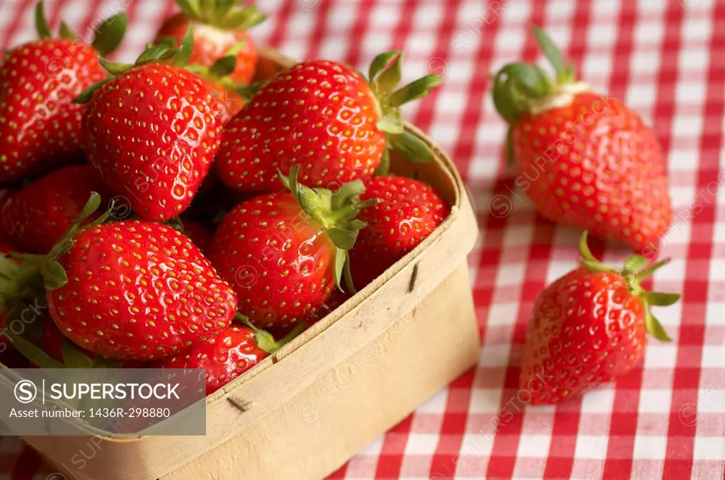 Punnet of fresh strawberries on gingham tablecloth