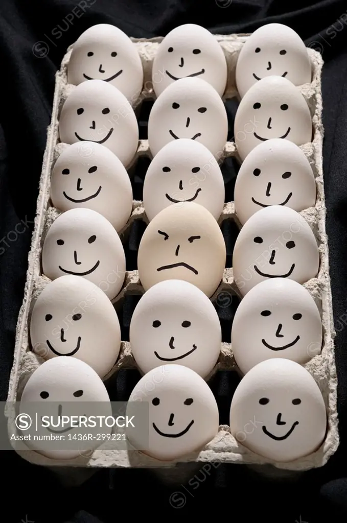 Package of backlit eggs on black cloth with smiling faces except for one grumpy sad face