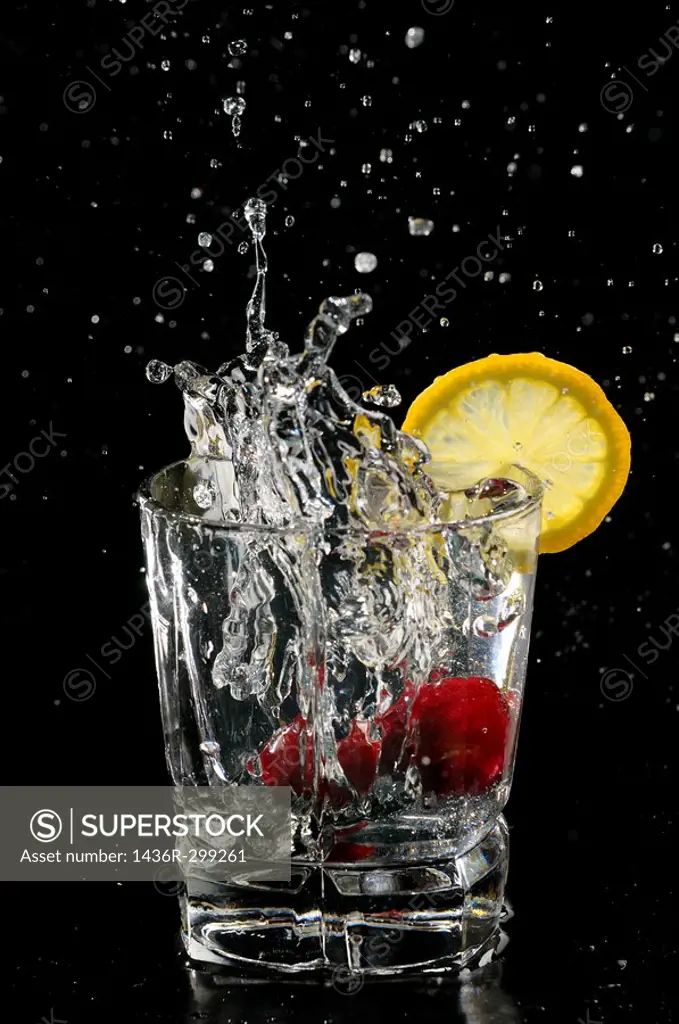 Cherries splashing into sparkling water glass with lemon slice on black background