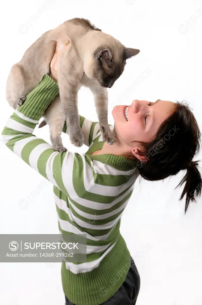 Smiling young girl lifting a Siamese cat to her face on a white background
