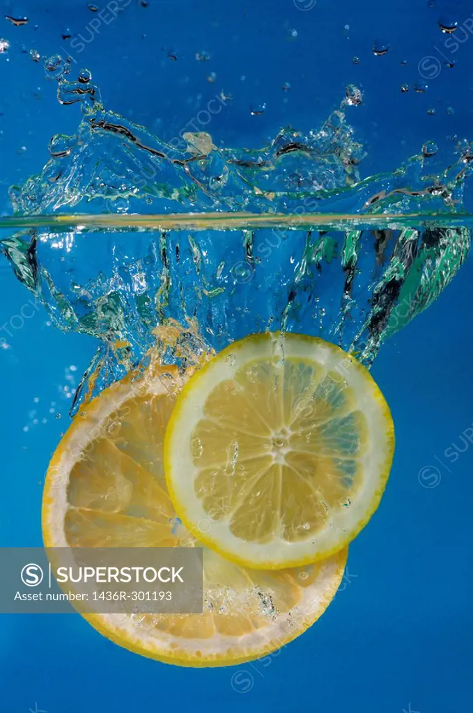 Lemon and grapefruit slices splashing into water with a blue background