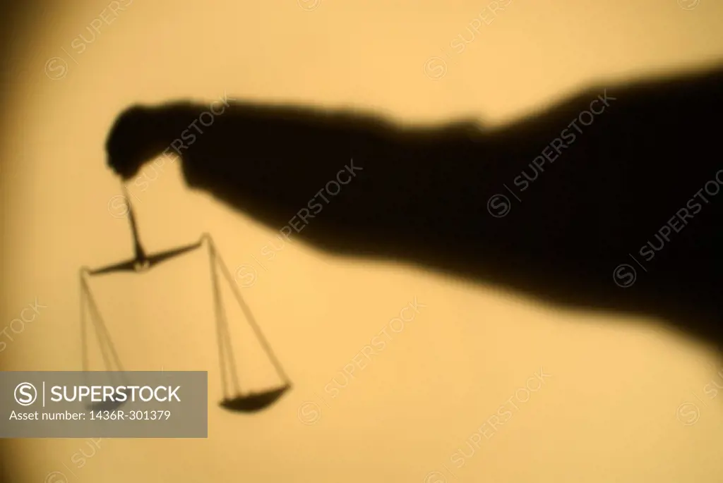 Shadow of a person´s arm holding out the Scales of Justice.