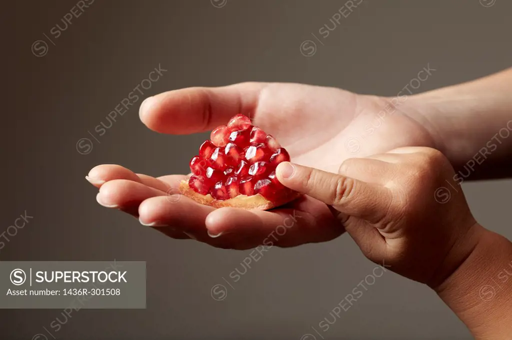 Woman hand holding a red piece of pomegranate on grey background with child hand touching it
