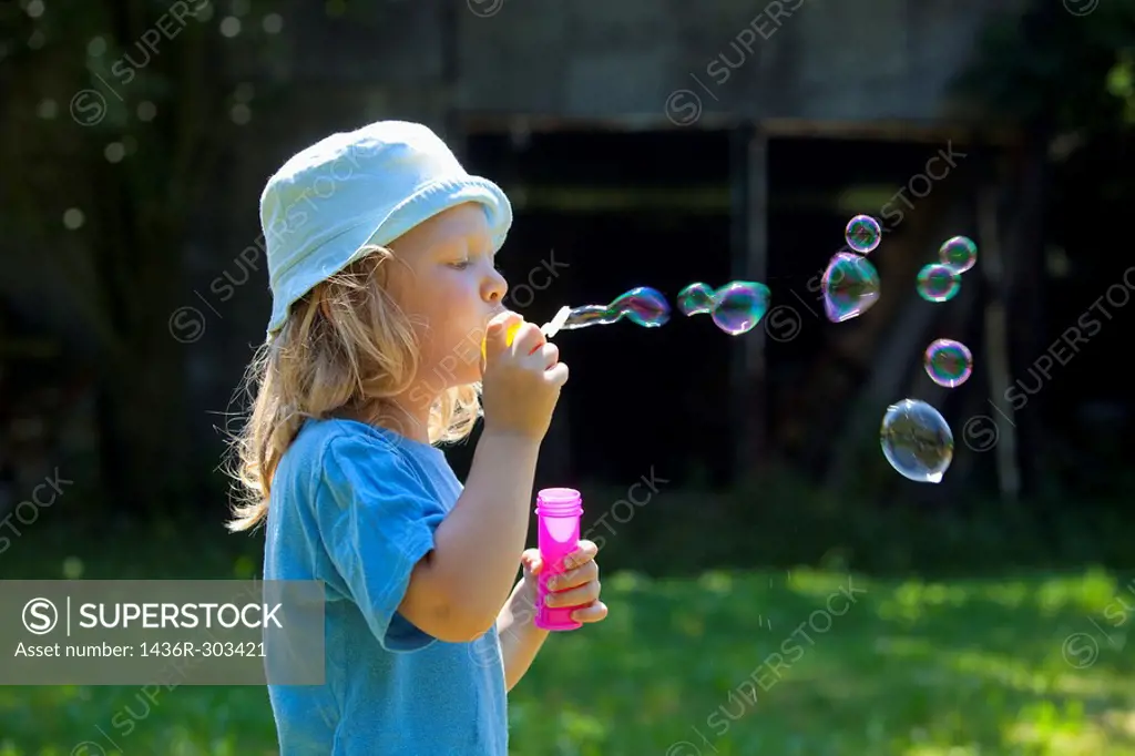 boy with long blond hair blowing soap bubbles outdoors