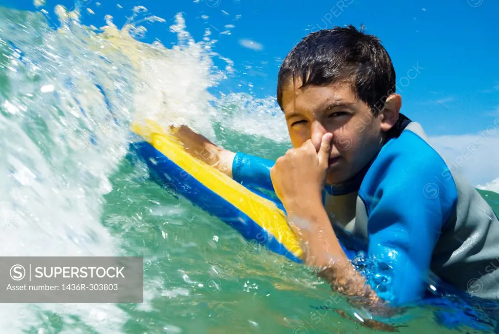 Young boy pinching his nose while surfing waves.