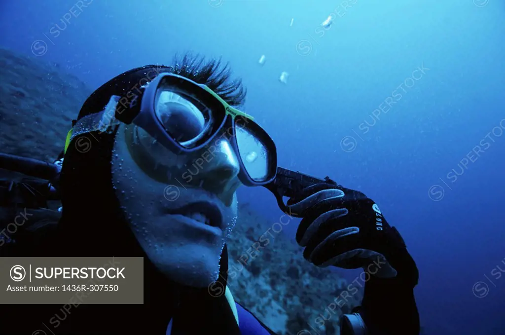 One scuba diver holding a gun to his head underwater.