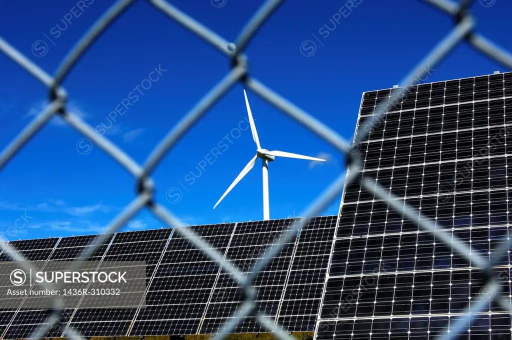 Security of installations for the generation of renewable energy, solar panels and a wind turbine behind a meshed security fence, solar power station ...