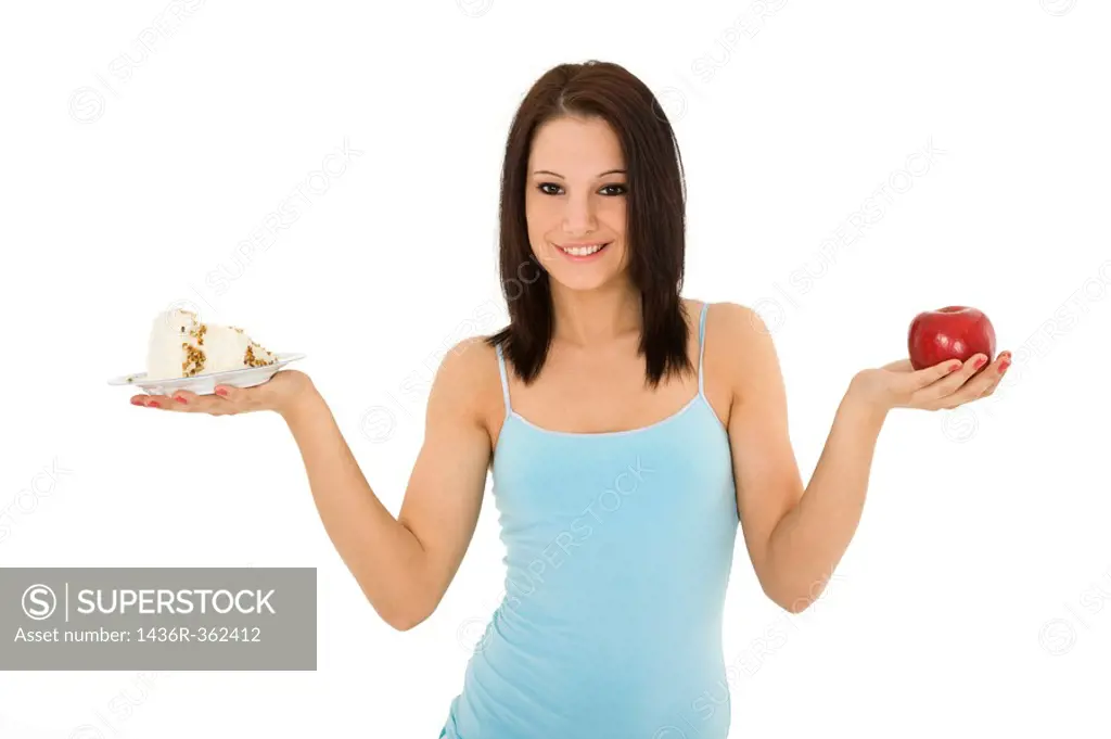 Caucasian woman holding an apple and slice of cake trying to decide which one to eat
