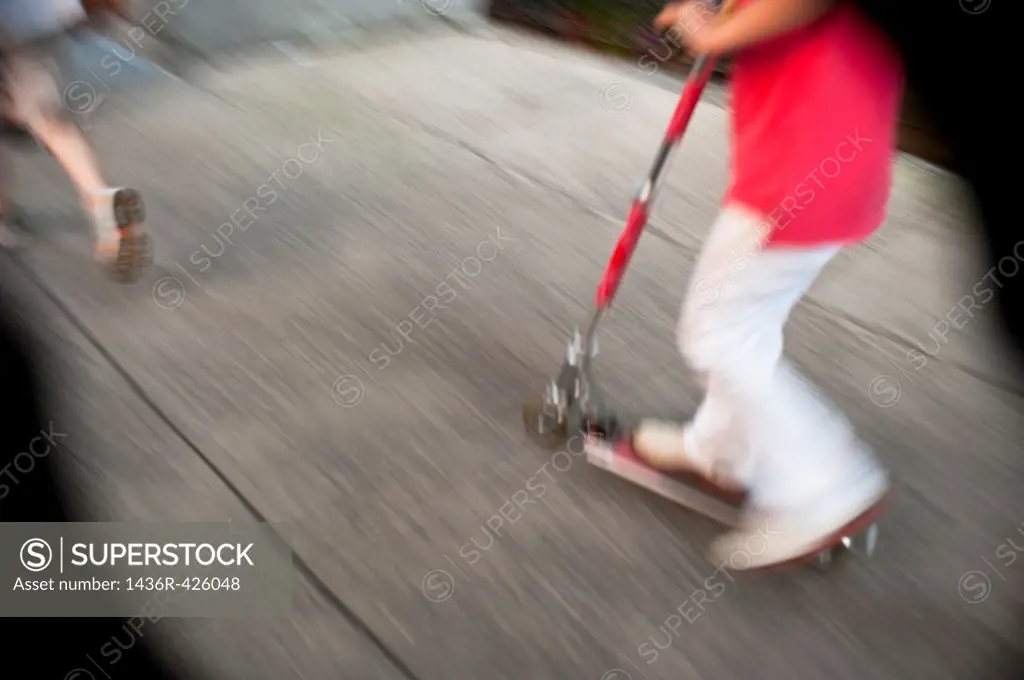A blurry photo of a child on a push scooter on a sidewalk in New York City, USA