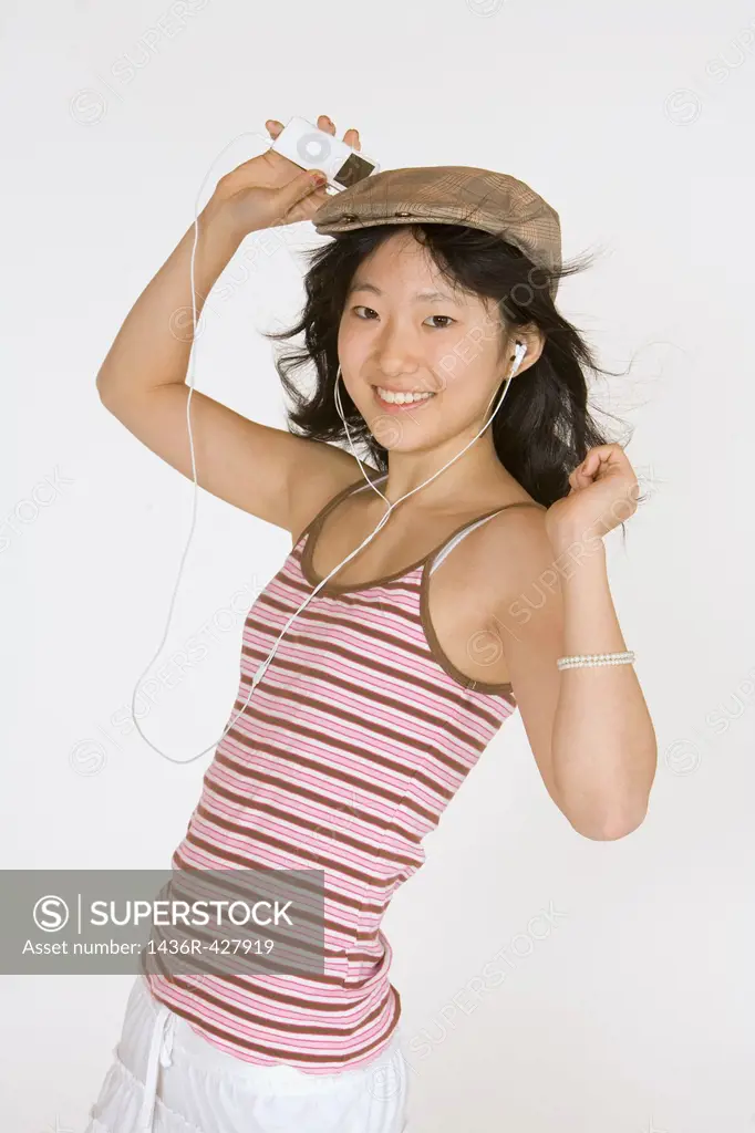 Asian teen listening to music on an MP3 playing on a white background