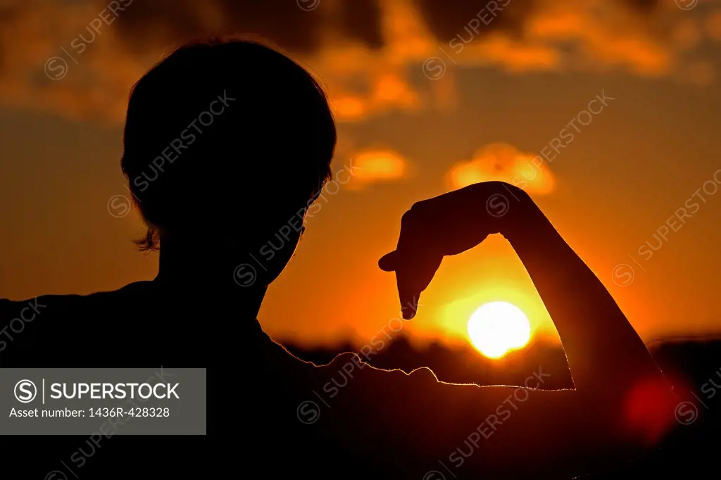 Woman silhouette holding arm around sun
