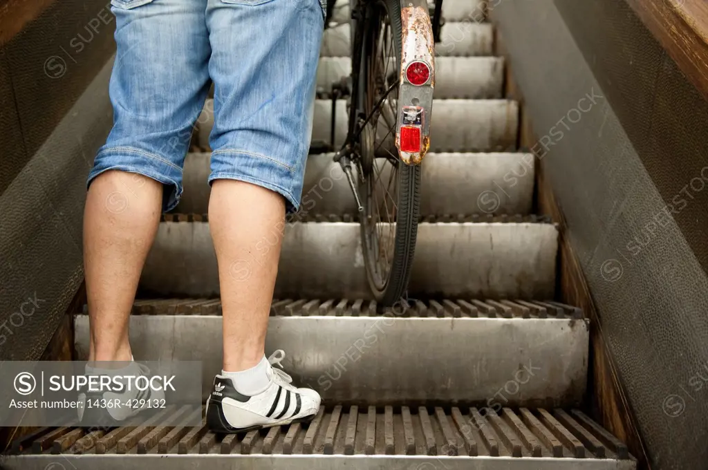 Rotterdam, Netherlands. Legs and feet of a pedestrian biker and bicycle rider, taking the historical wooden escalator in Maastunnel, beneath river Nie...