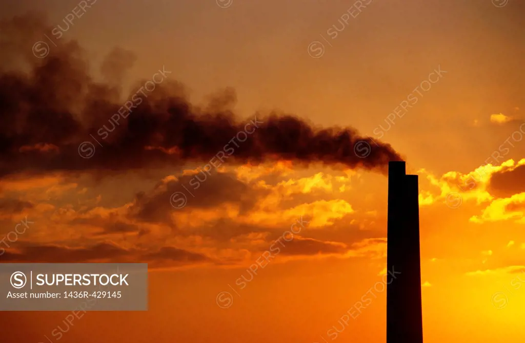 Silhouetted smoking chimney at sunset, Berre, France