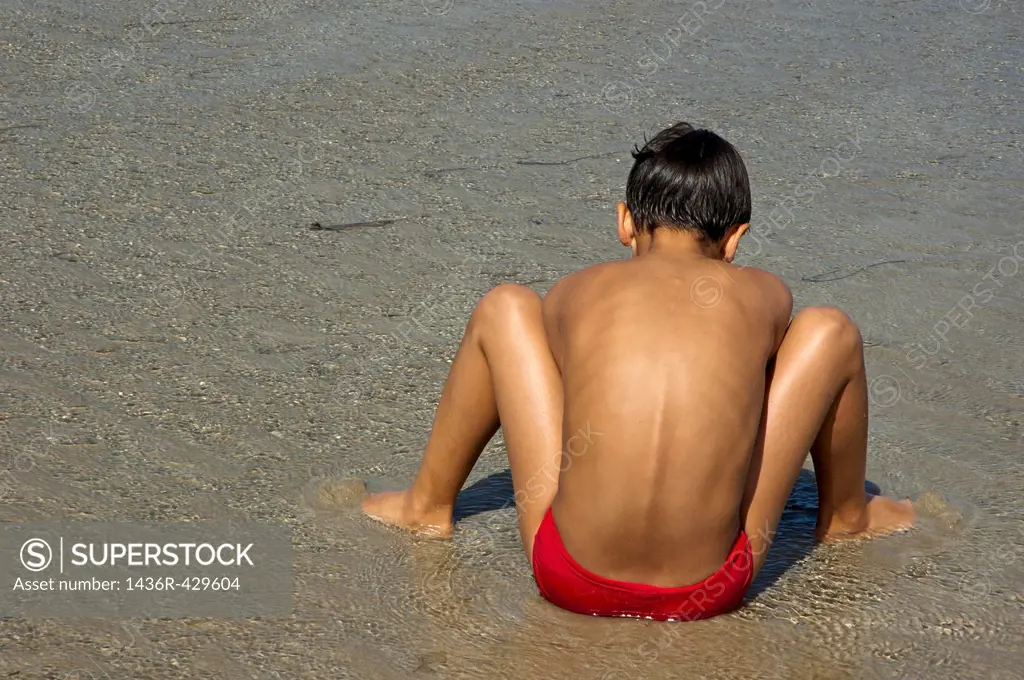 Boy digging in the wet sand at Penguen Beach, Saint-Cast-le-Guildo, France.