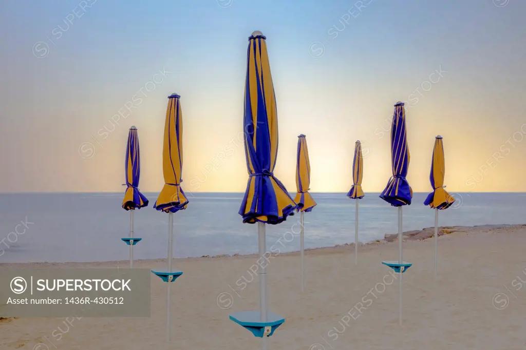 closed umbrellas at the beach of the Mediterranean Sea at sunset, Italy