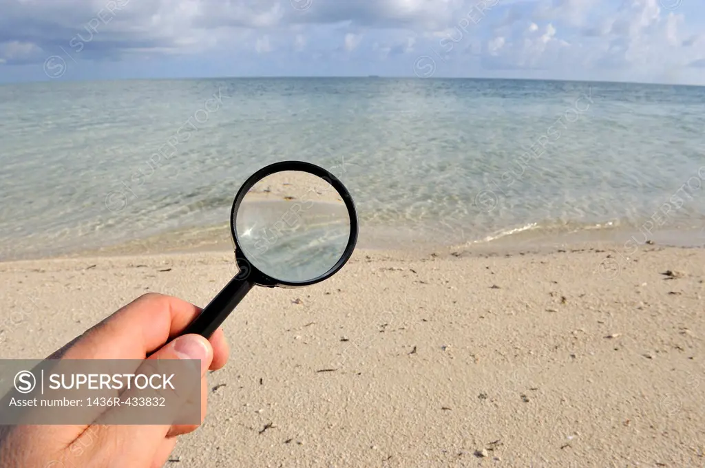 Hand holding a magnifying glass on a tropical beach, sland of Borneo, Sabah State, Malaysia