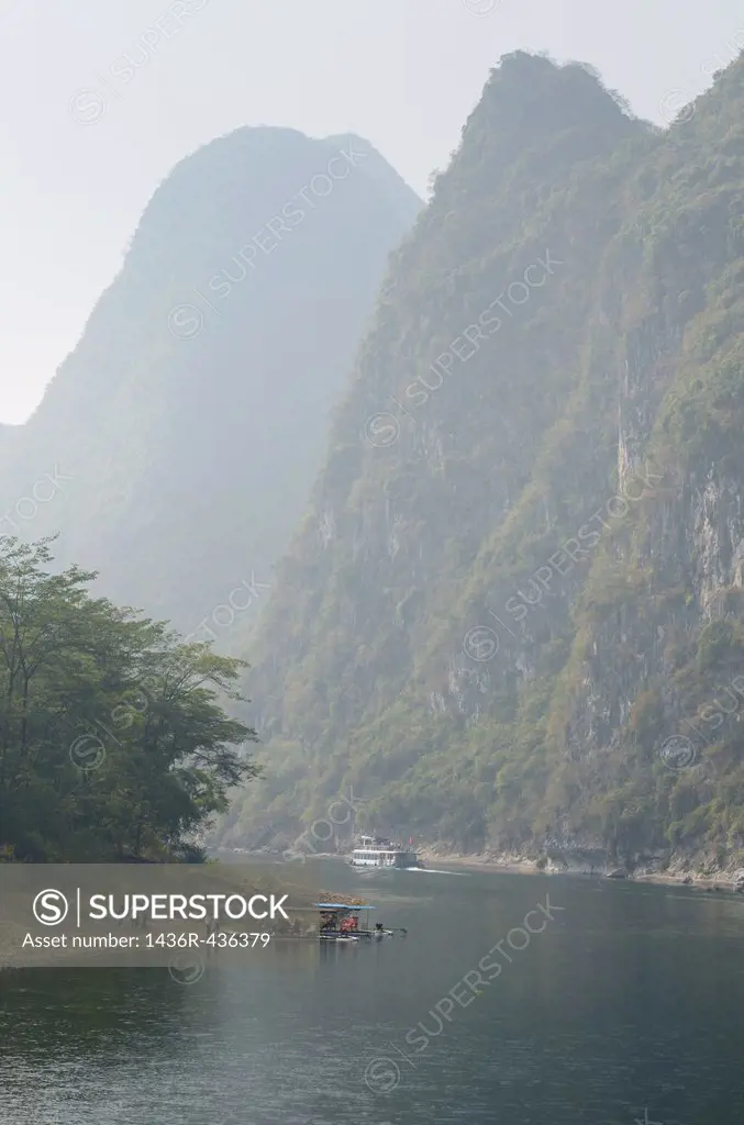 Cruise ship and sightseeing rafts on the hazy Li River in China among the tall karst peaks of Guangxi