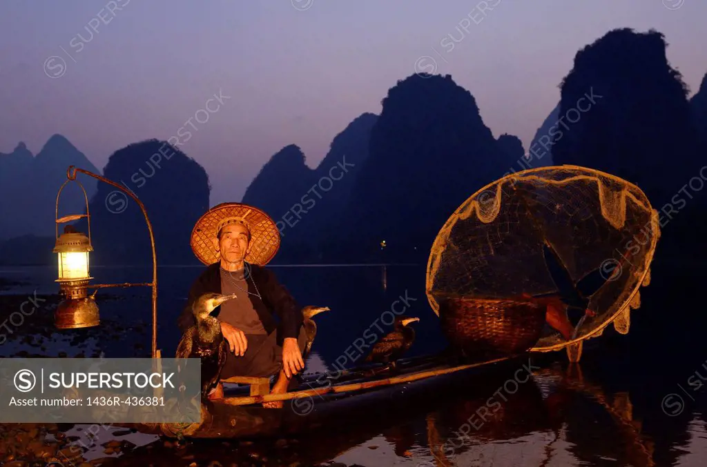Fisherman with cormorants on bamboo raft at dawn on the shore of the Li river Yangshuo China