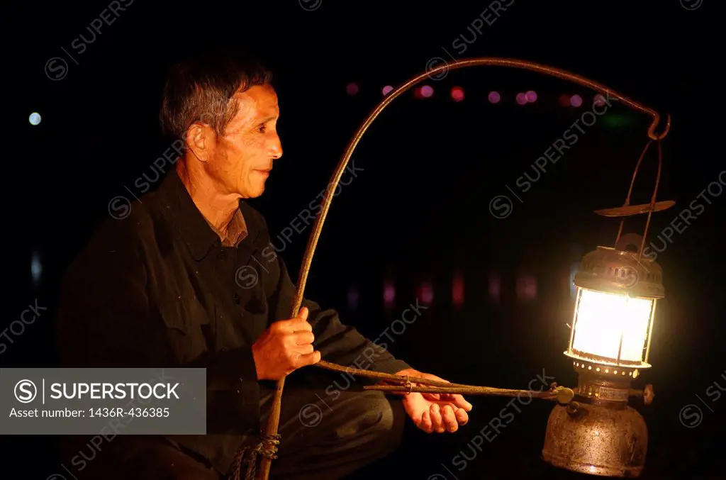 Cormorant fisherman placing his lamp on his raft in early morning darkness on the Li river Yangshuo China