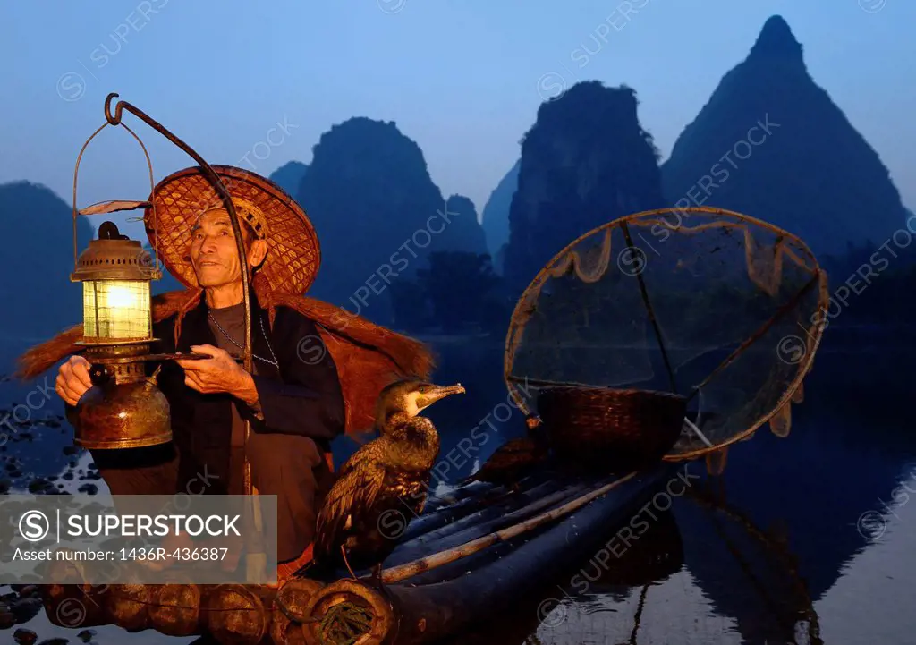 Fisherman with lantern on a bamboo raft with cormorants at dawn on the shore of the Li river Yangshuo China