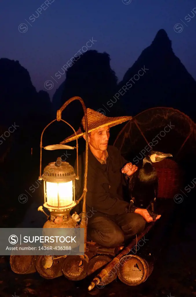 Chinese cormorant fisherman holding a bird on a bamboo raft with lantern at dawn on the Li river Yangshuo China