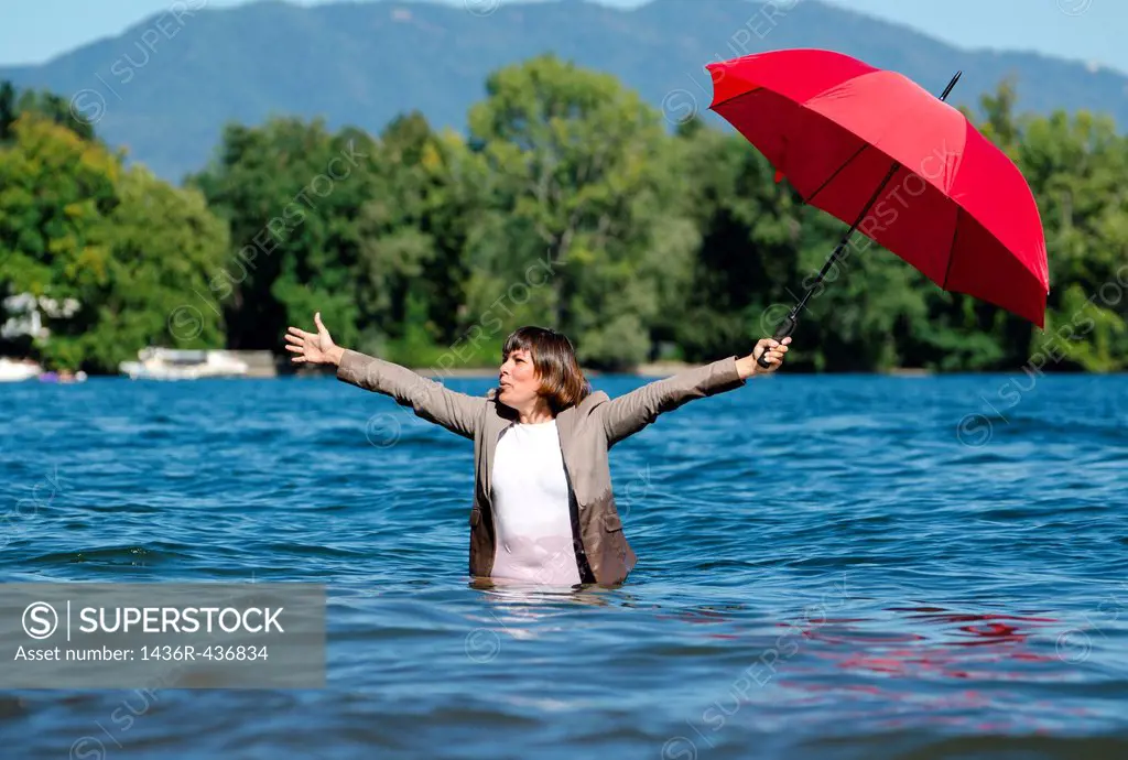 Woman standing in the water with a red umbrella and with a suit
