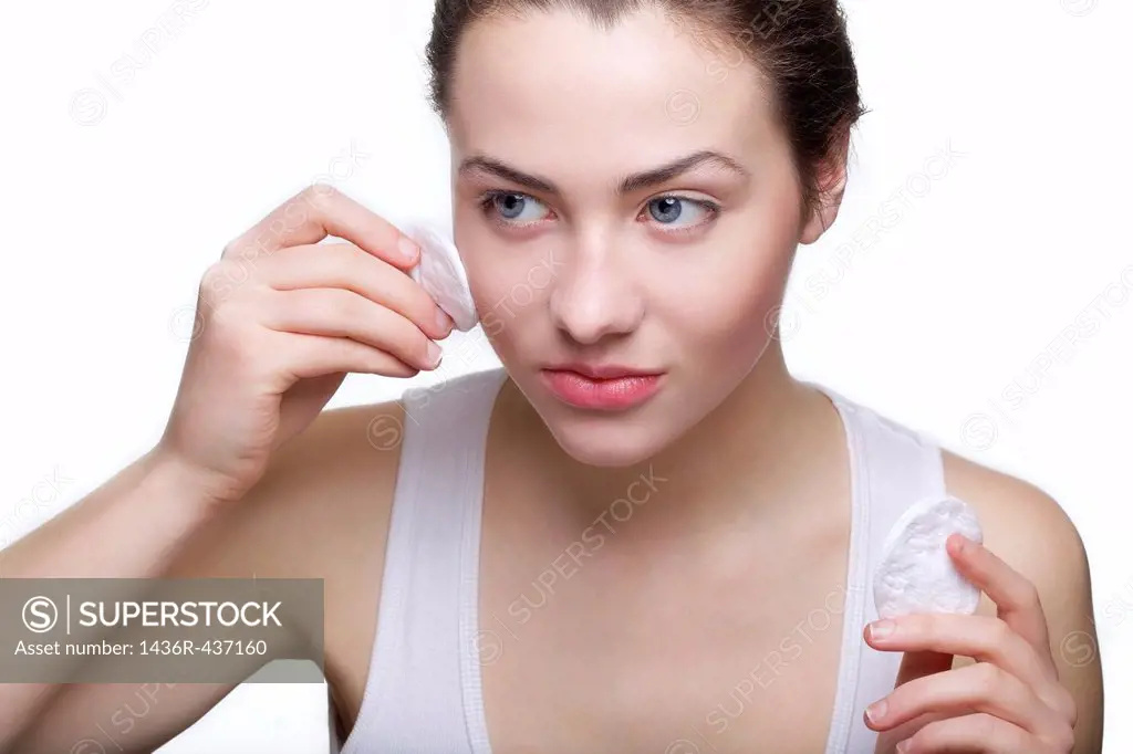 Beautiful young woman removing make up with cotton swab pad