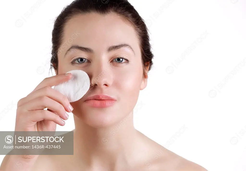 Beautiful young woman removing make up with cotton swab pad