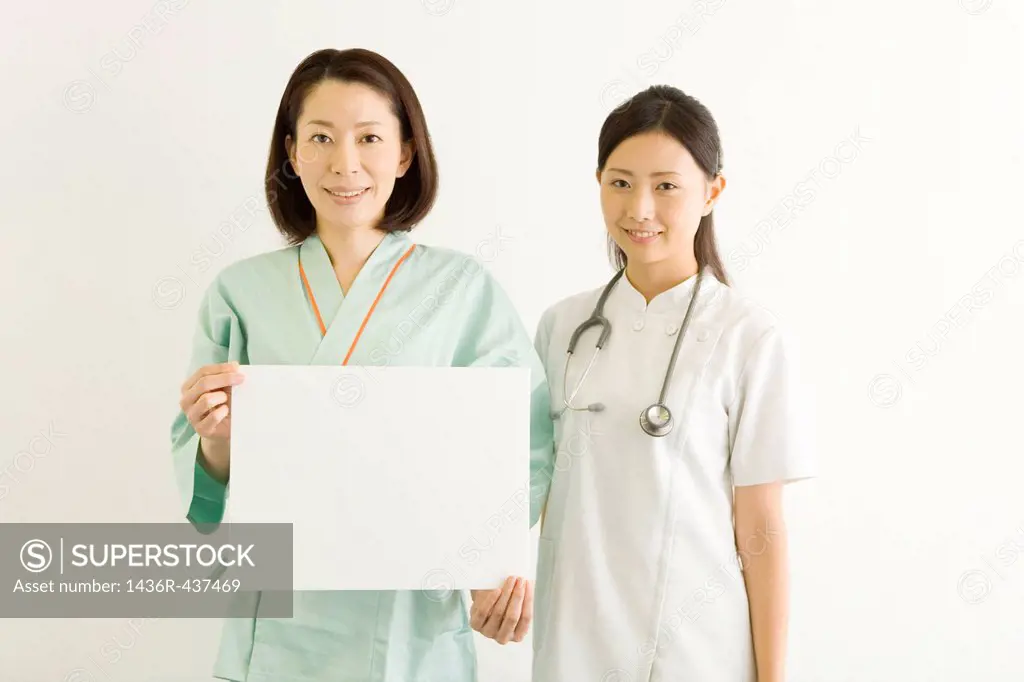 Female doctor and mid adult woman in examination gown showing board