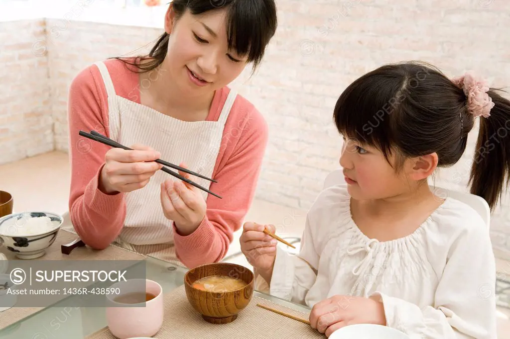Mother teaching daughter how to use chopsticks