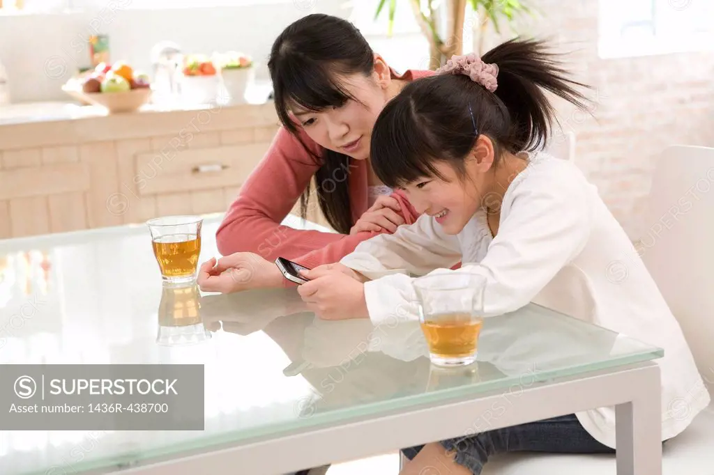 Mother and daughter looking smartphone at dining table