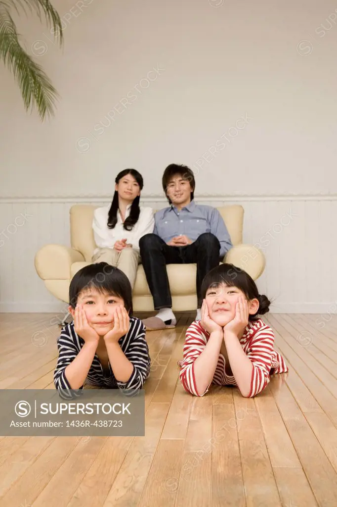 Parents sitting on sofa and children lying on wooden floor