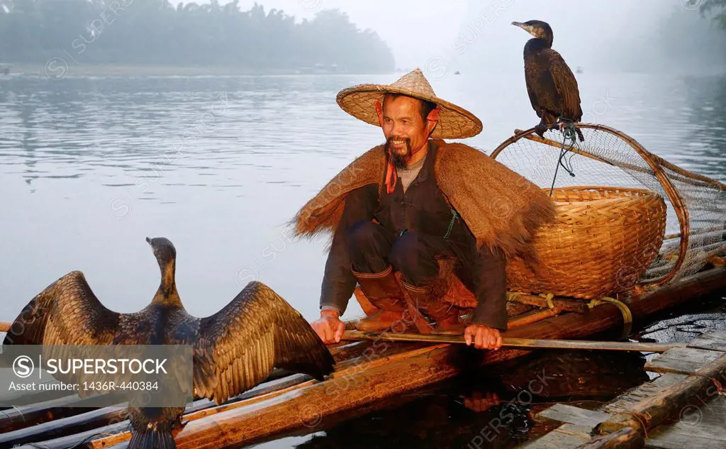 Smiling cormorant fisherman with birds on a bamboo raft on the Li river at dawn Xingping China