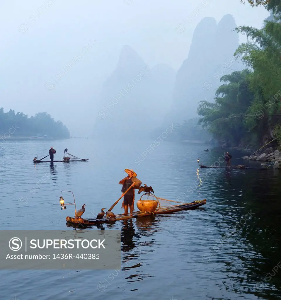 Cormorant fishermen in mist at dawn on the Li river with Karst mountain peaks near Xingping China