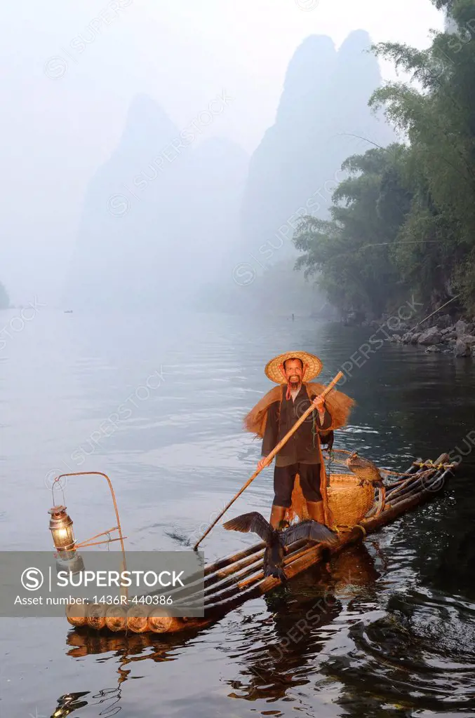 Cormorant fisherman paddling bamboo raft on the Li river with Karst mountain peaks near Xingping China