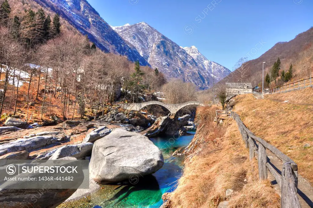 Roman bridge over a river with snow-capped mountain in autumn