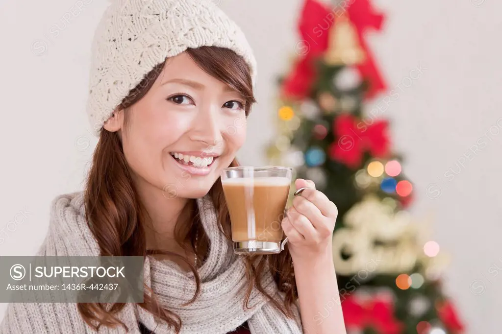 Young Woman Holding Cappuccino Cup in front of Christmas Tree