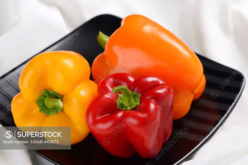 Red yellow and orange bell peppers on a square black plate